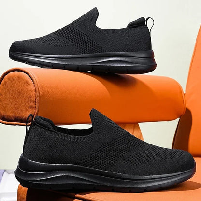 Black slip-on mesh sneakers for women with cushioned sole, shown from side and front angles on orange surface