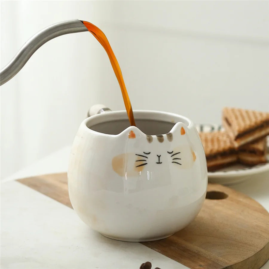 White ceramic cat mug with orange ears and tail handle being filled with coffee on wooden board
