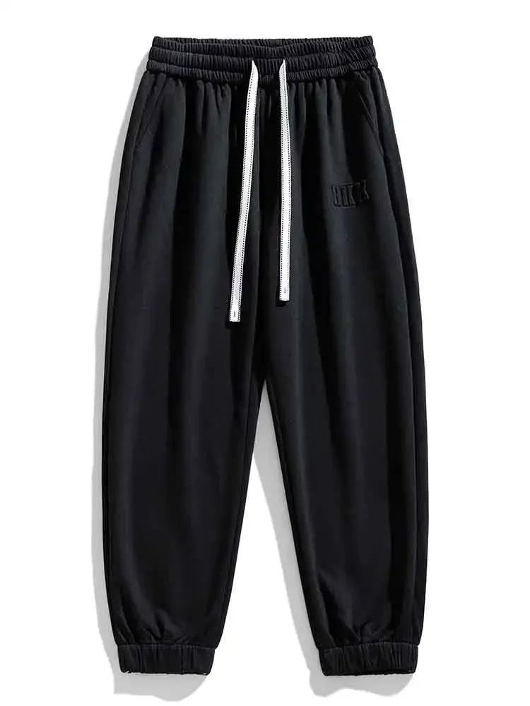 Black men's drawstring sweatpants with elastic waistband, white cord, ribbed cuffs, and embroidered logo detail.