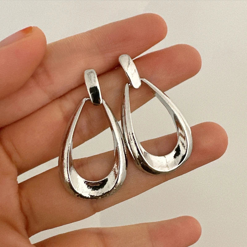 Silver teardrop hoop drop earrings held in a woman's hand, showing open oval design with polished metallic finish