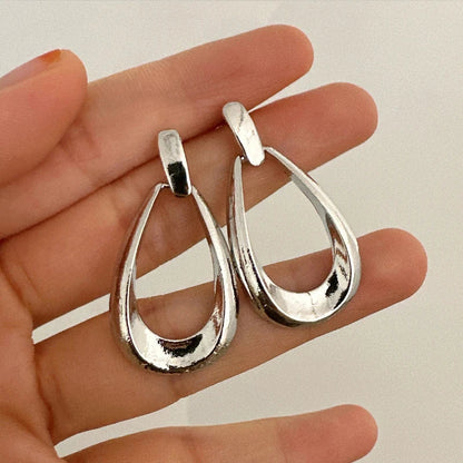 Silver teardrop hoop drop earrings held in a woman's hand, showing open oval design with polished metallic finish