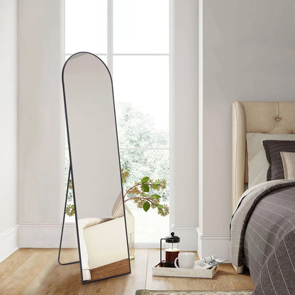 Arched full length standing mirror with black metal frame leaning against white wall in modern bedroom