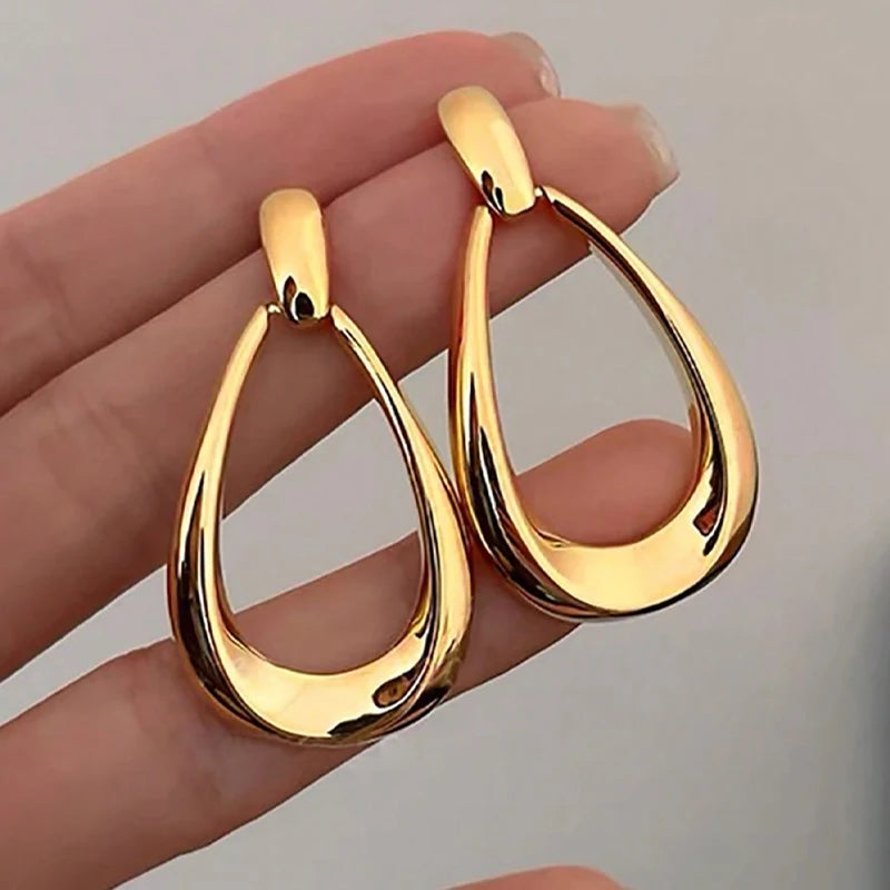 Vanya gold-tone teardrop drop earrings with hollow open design, shown held in hand to display size and shine.