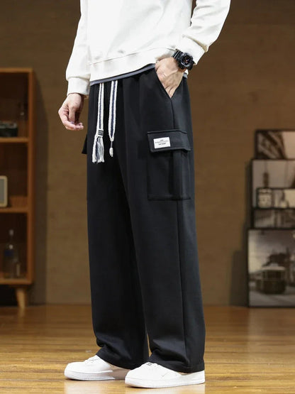Men's black relaxed fit cargo sweatpants with side pocket patch, drawstring waist, worn with white sneakers and sweatshirt.