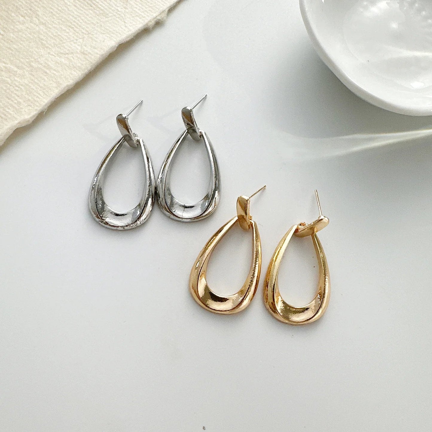 Vanya teardrop drop earrings in gold and silver tones with stud backs, displayed side by side on white surface