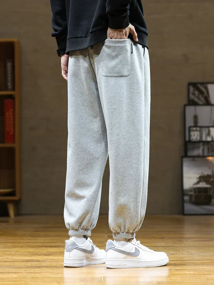 Men's gray drawstring sweatpants with elastic cuffs and back pocket worn with white sneakers