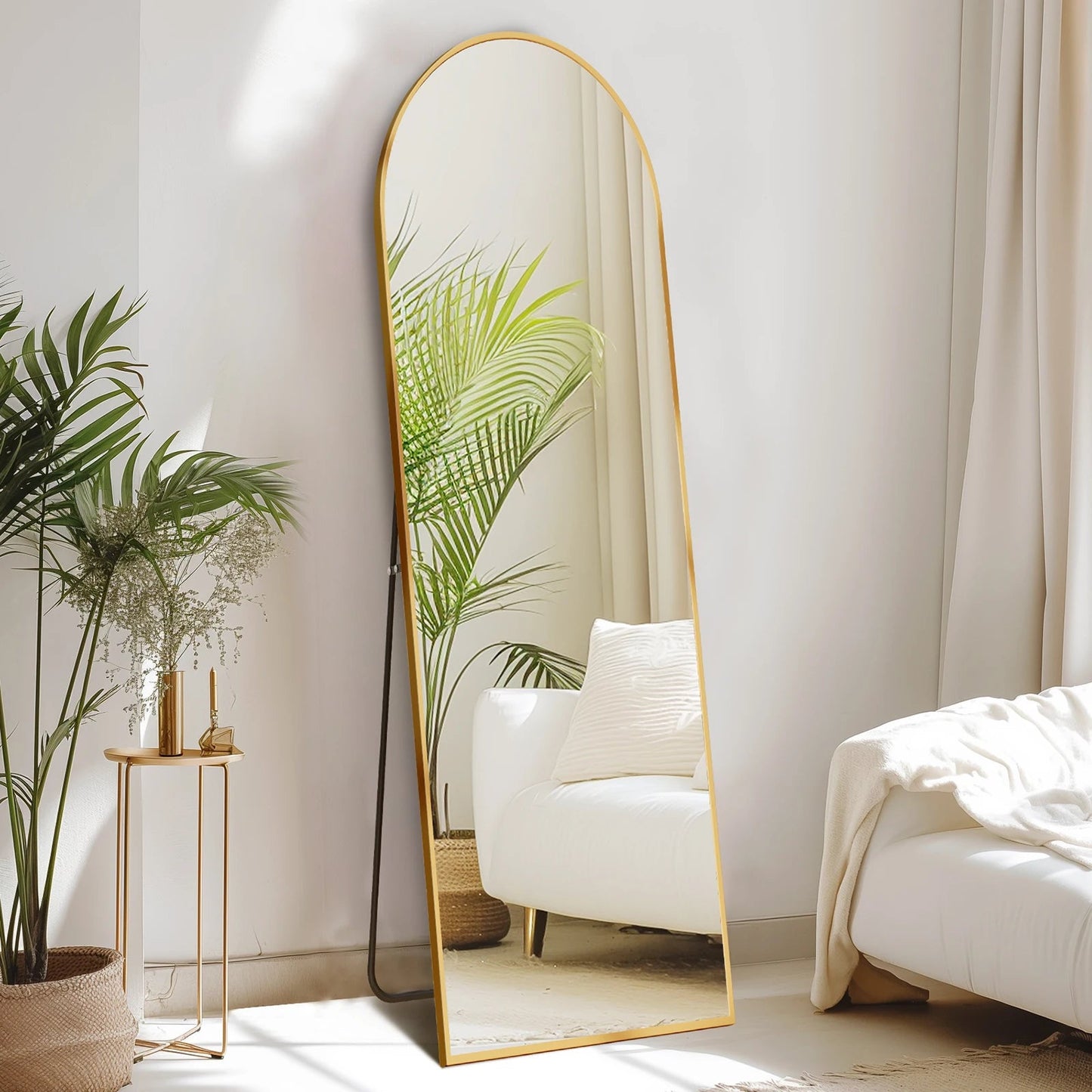 Arched full length floor mirror with gold metal frame in modern minimalist bedroom with white chair and plants