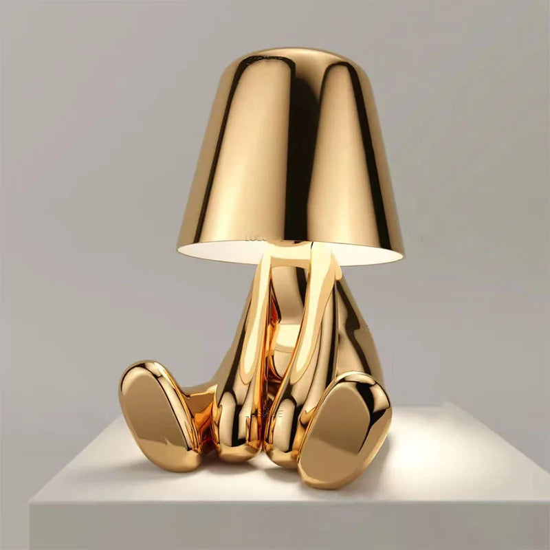Gold metallic sitting figurine desk lamp with lampshade head, dimmable decorative ambient light on white pedestal