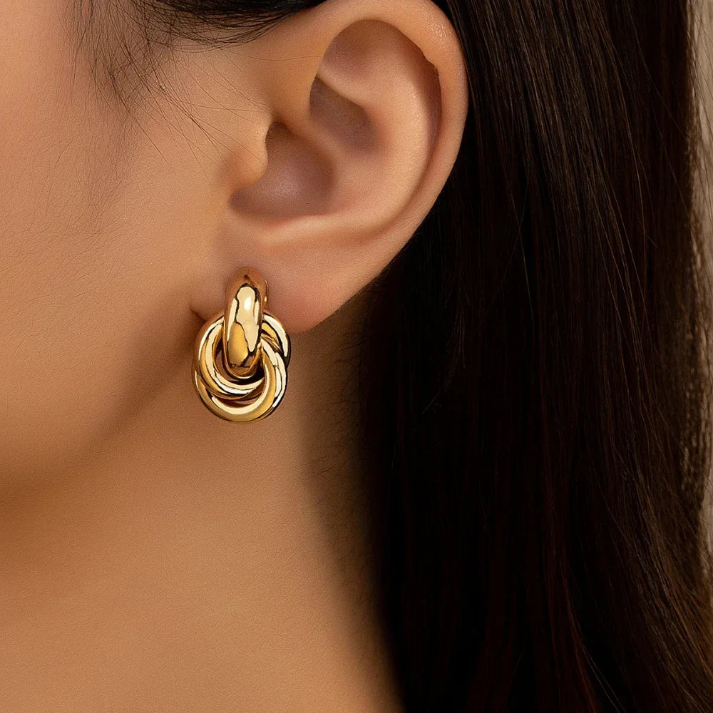 Gold tone interlocked knot hoop earrings worn on ear, chunky twisted metal design statement jewelry for women