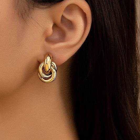 Gold tone interlocked knot hoop earrings worn on ear, chunky twisted metal design statement jewelry for women