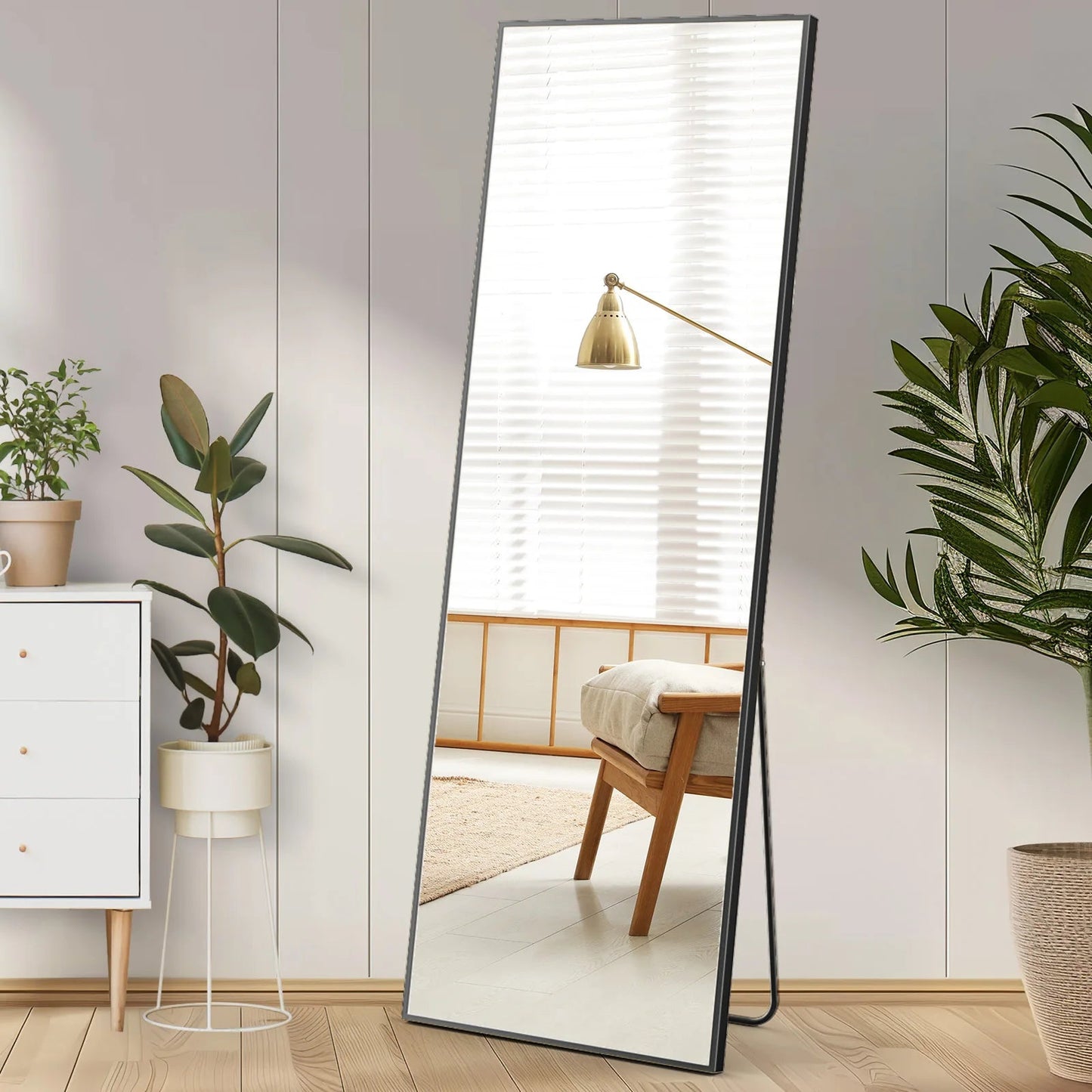 Full-length rectangular standing mirror with black metal frame leaning against white wall in modern bedroom setting.