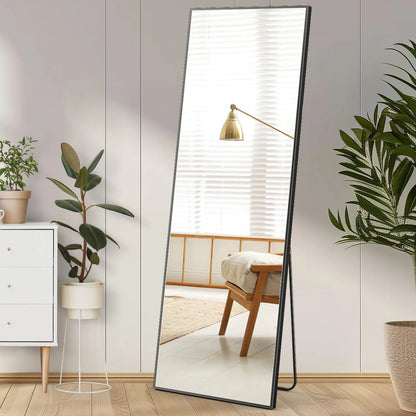 Full-length rectangular standing mirror with black metal frame leaning against white wall in modern bedroom setting.