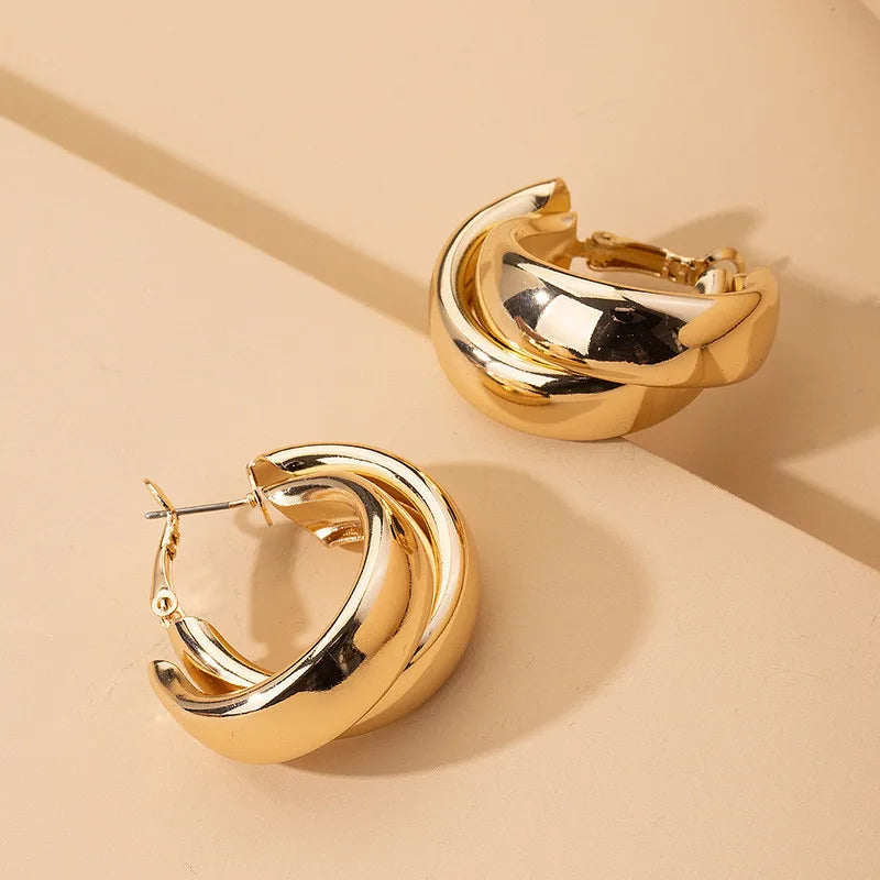 Chunky twisted gold-tone hoop earrings with layered double-ring design, shown as a pair on beige surface