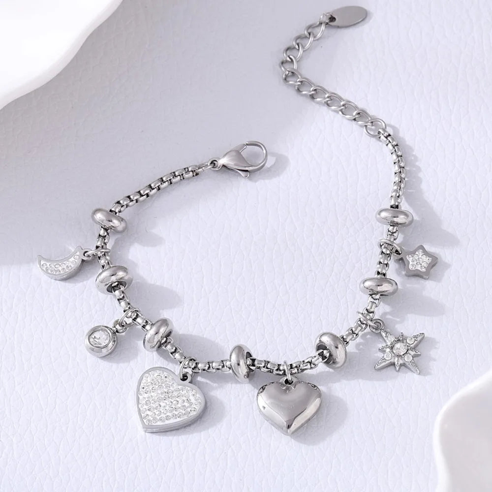 Silver charm bracelet featuring crystal heart, moon, star pendants, and rhinestone accents on a box chain with lobster clasp