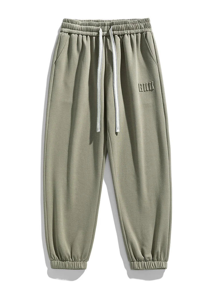 Sage green men's tapered knit joggers with elastic waistband, white drawstring, side pockets, and ribbed ankles.