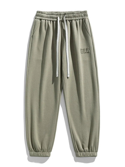 Sage green men's tapered knit joggers with elastic waistband, white drawstring, side pockets, and ribbed ankles.