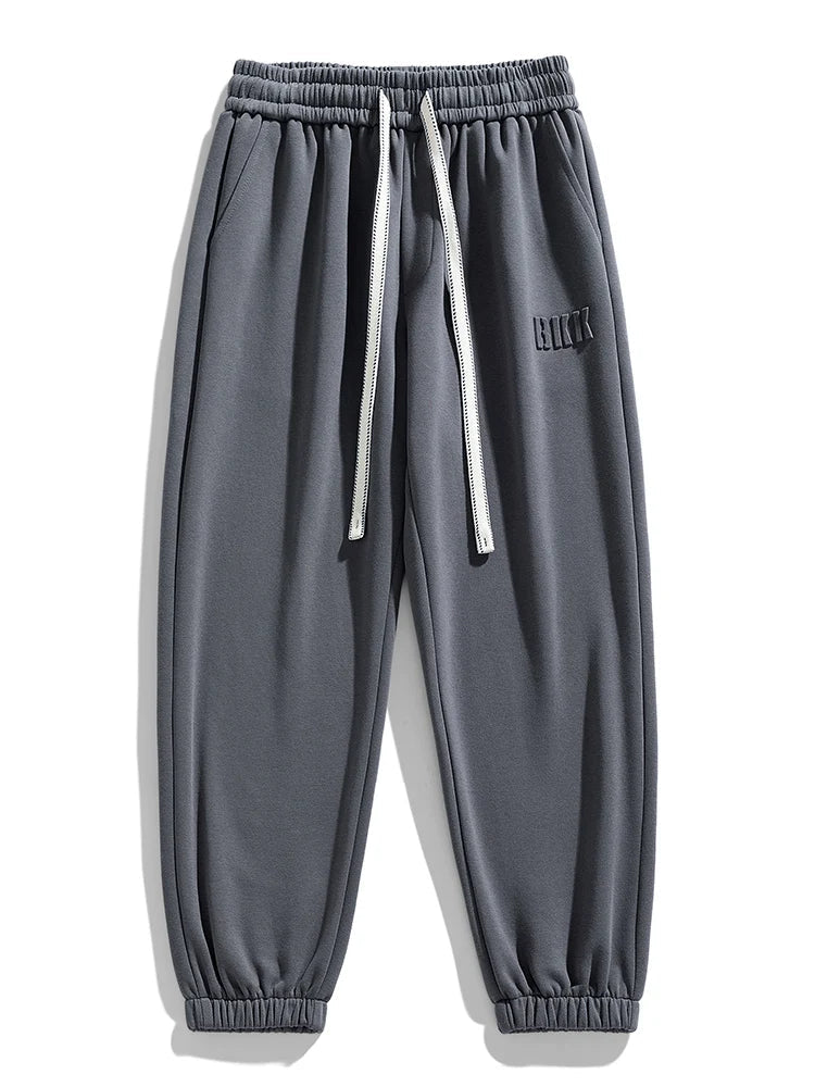Men's gray tapered knit joggers with elastic waistband, white drawstring, side pockets, and ribbed ankle cuffs.
