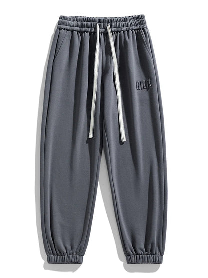 Men's gray tapered knit joggers with elastic waistband, white drawstring, side pockets, and ribbed ankle cuffs.
