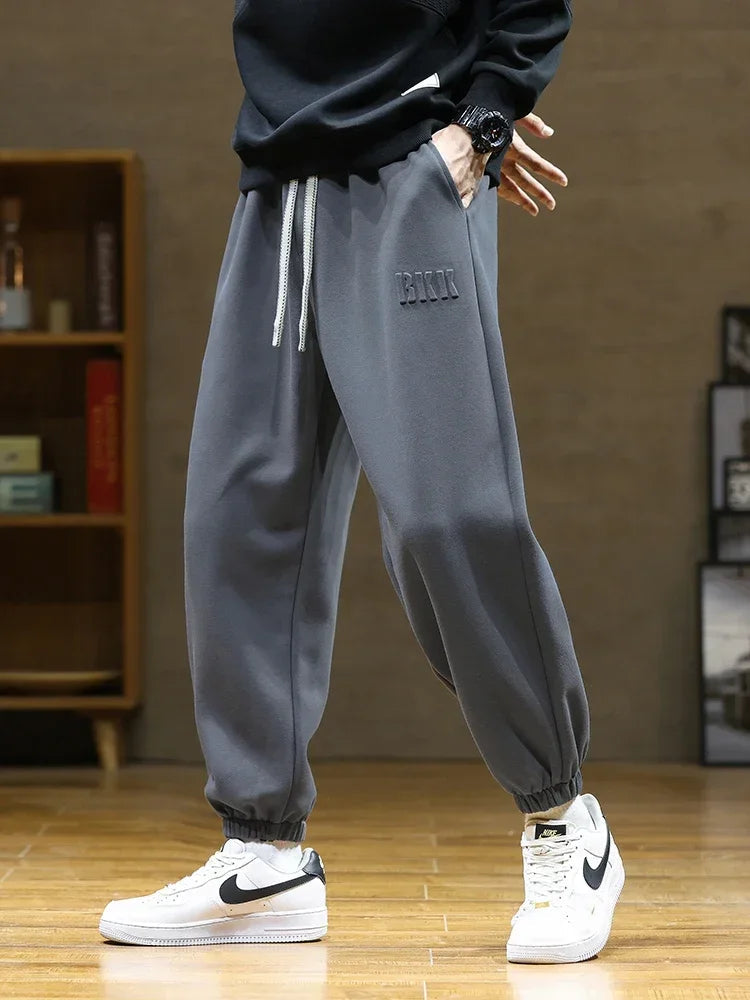 Men's gray drawstring jogger sweatpants with elastic cuffs, worn with white Nike Air Force 1 sneakers and black sweatshirt.